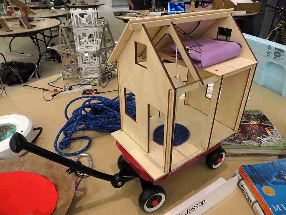 Wooden playhouse structure on wheels with purple cushion and electronic components in workshop.