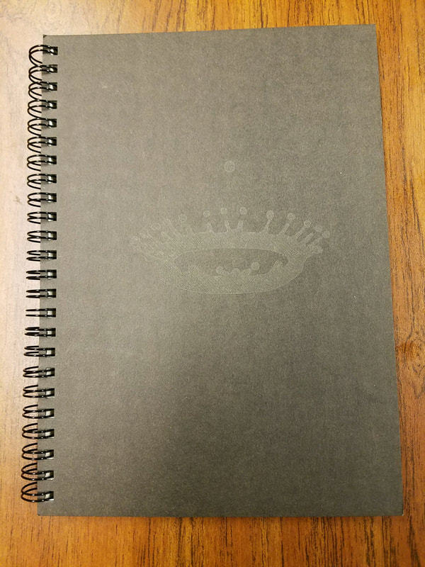 Spiral-bound notebook with gray cover and eye illustration on wooden surface