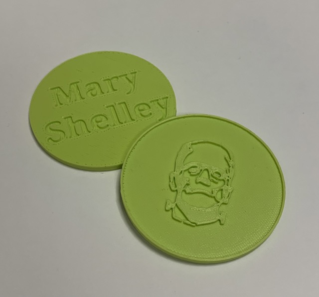 a 3D printed coin showing an image of Frankenstein's monster embossed on one side and "Mary Shelley" debossed on the reverse.