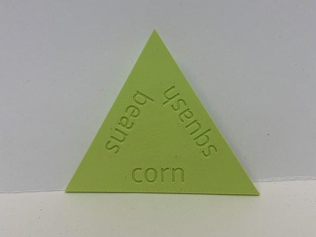 a 3D printed triangle with the text "corn", "squash", and "beans" debossed into the surface.