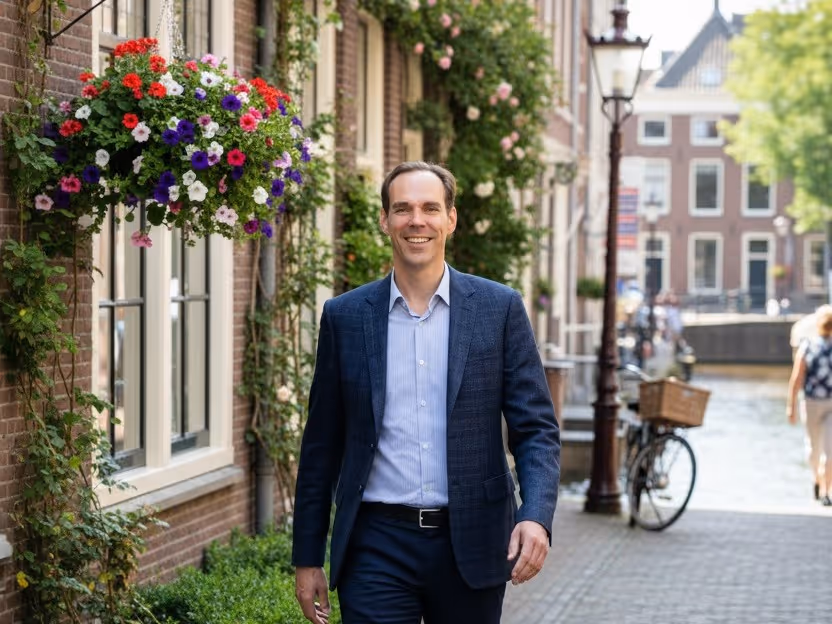 Pallieter Koopmans smiling in a blazer walking on a cobblestone street with flowers and a canal in the background.