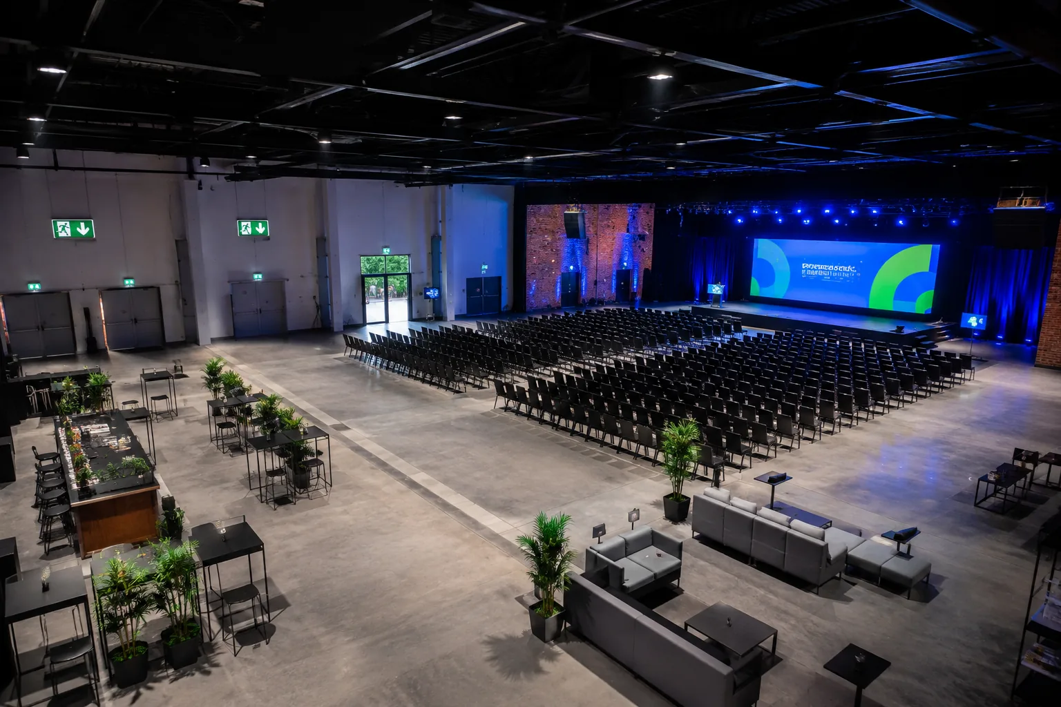 Pusta sala konferencyjna z rzędami krzeseł i oznaczonymi wyjściami ewakuacyjnymi