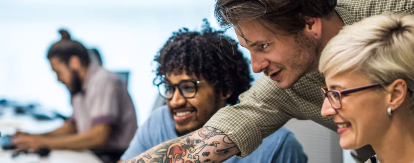 A team of cybers security experts cooperating while analysing a security event. One of them is pointing at a computer screen.