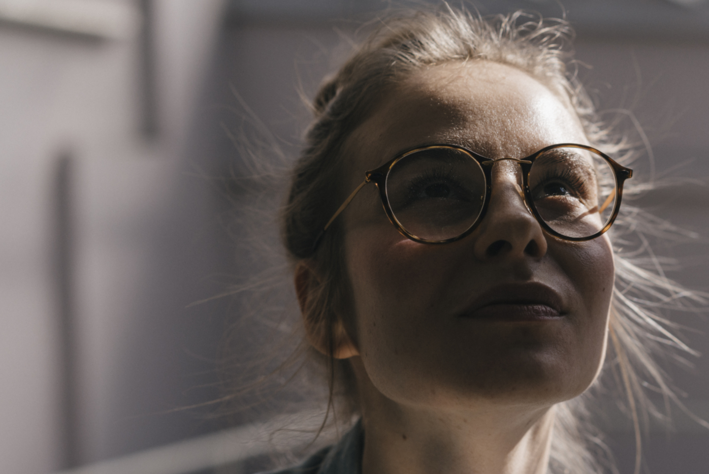 Young woman with glasses looking up, with sunlight on her face.