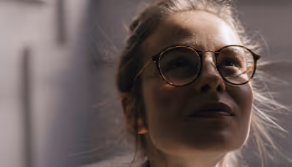 Young woman with glasses looking up, with sunlight on her face.