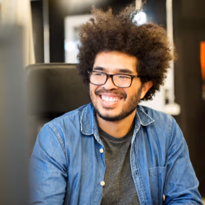 A male cyber security analyst smiling while looking at a computer screen.