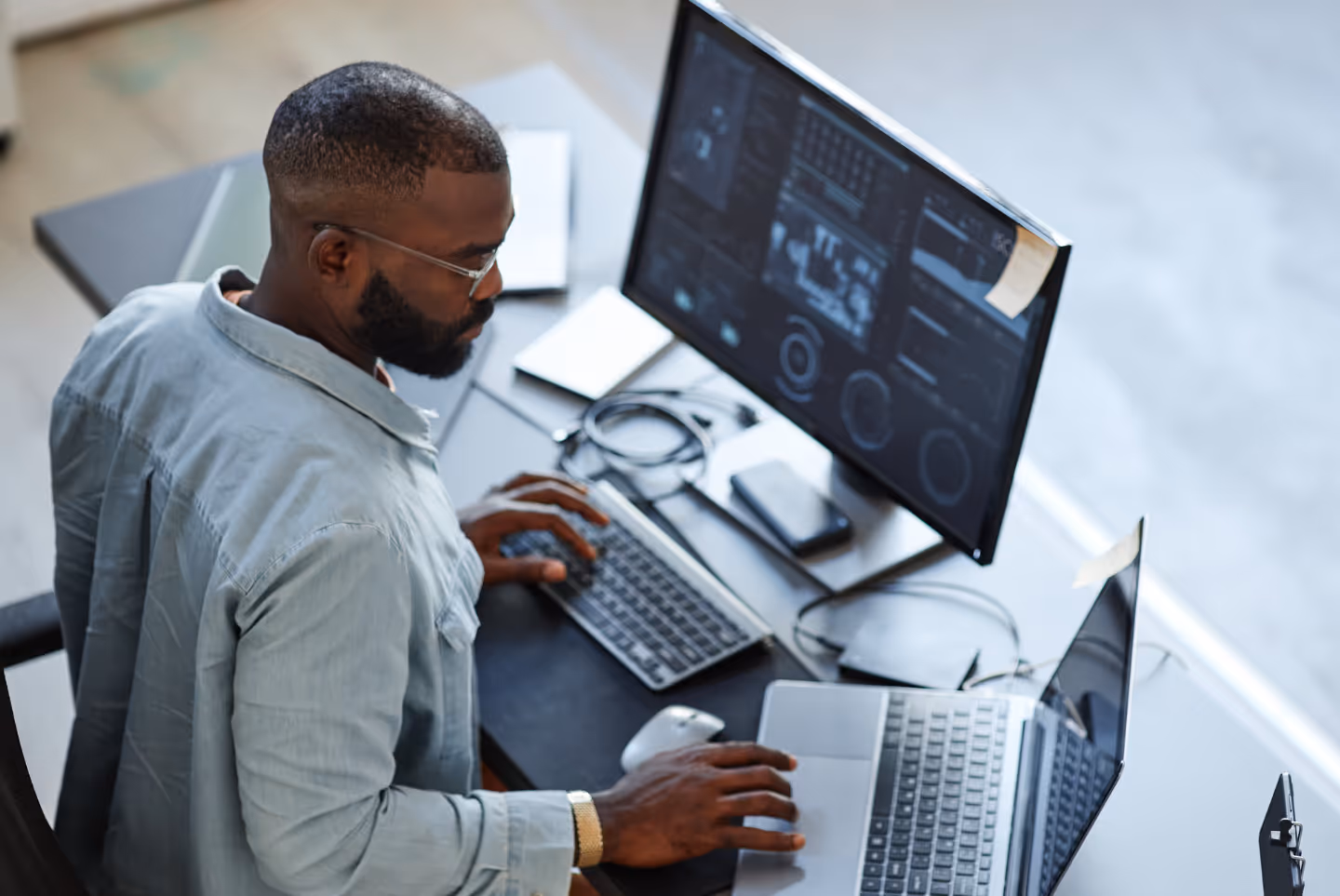 High angle view of a cyber security analyst working across a computer screen and laptop
