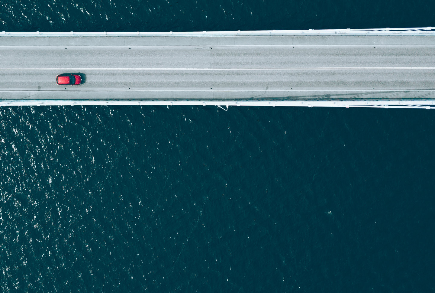A red car travelling across a bridge, with water below.