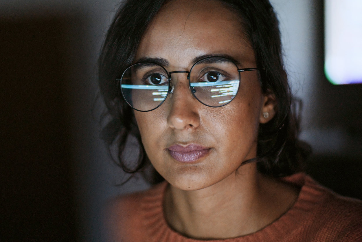 Close up image of a woman with glasses looking at screen, with the screen reflecting the glasses.