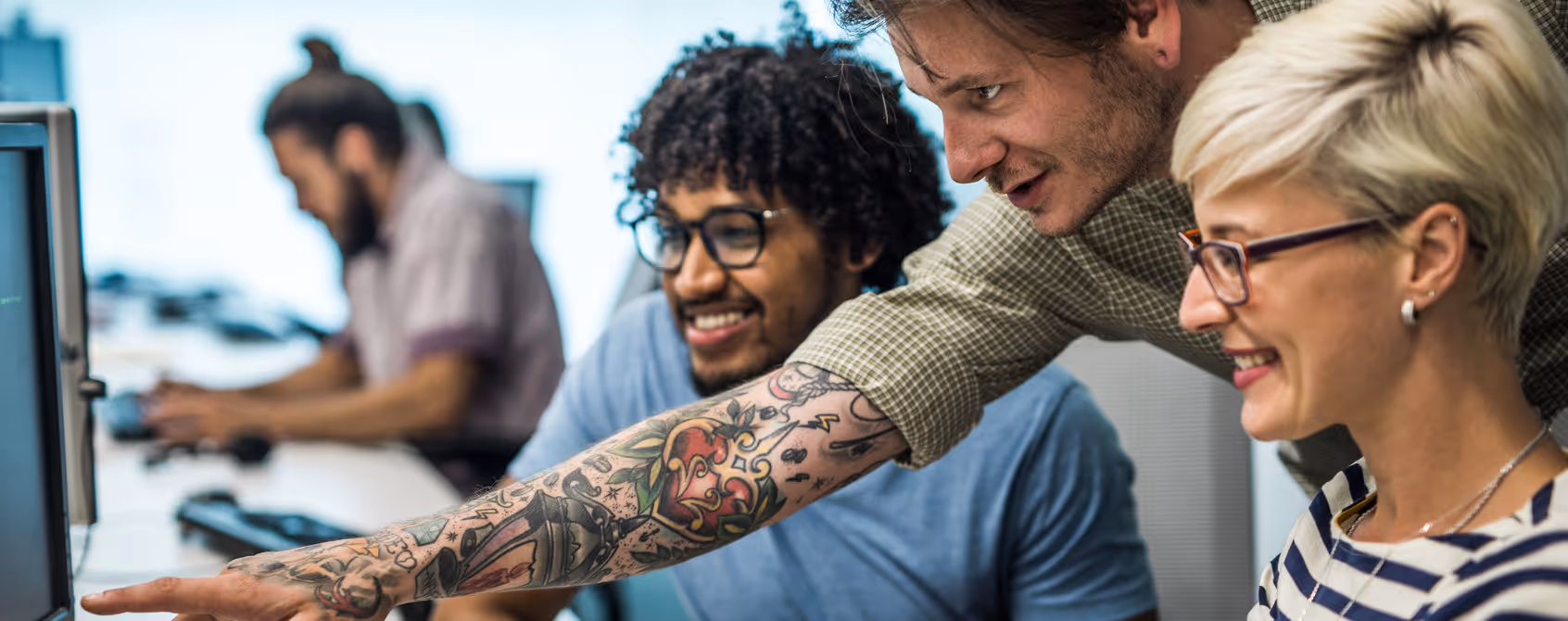 A team of cybers security experts cooperating while analysing a security event. One of them is pointing at a computer screen.