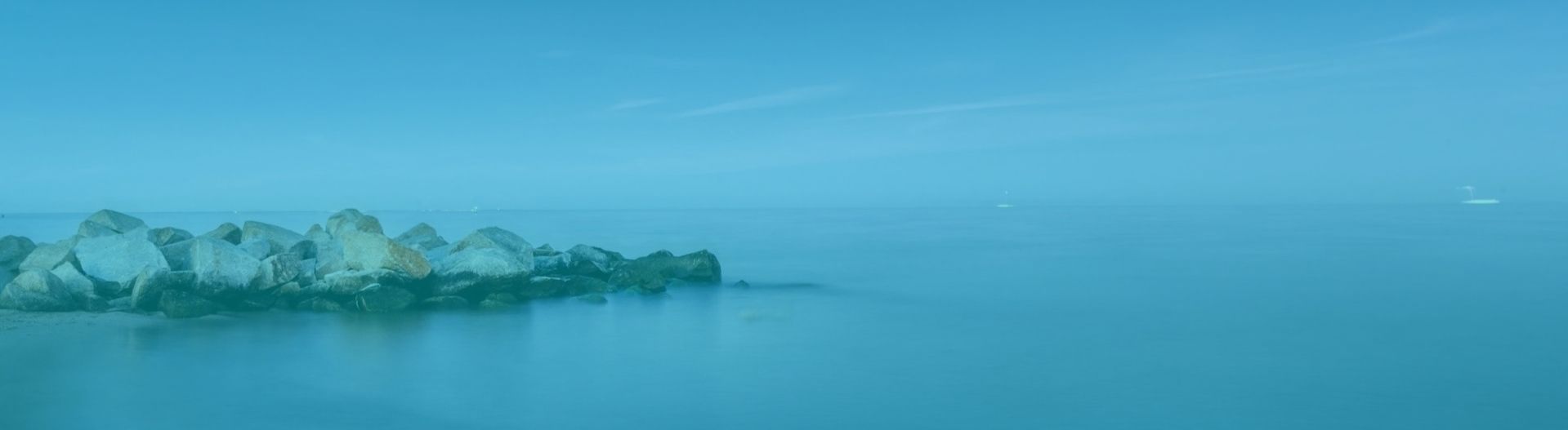 A rocky breakwater extending into a calm body of water under a moody, bluish-toned sky.