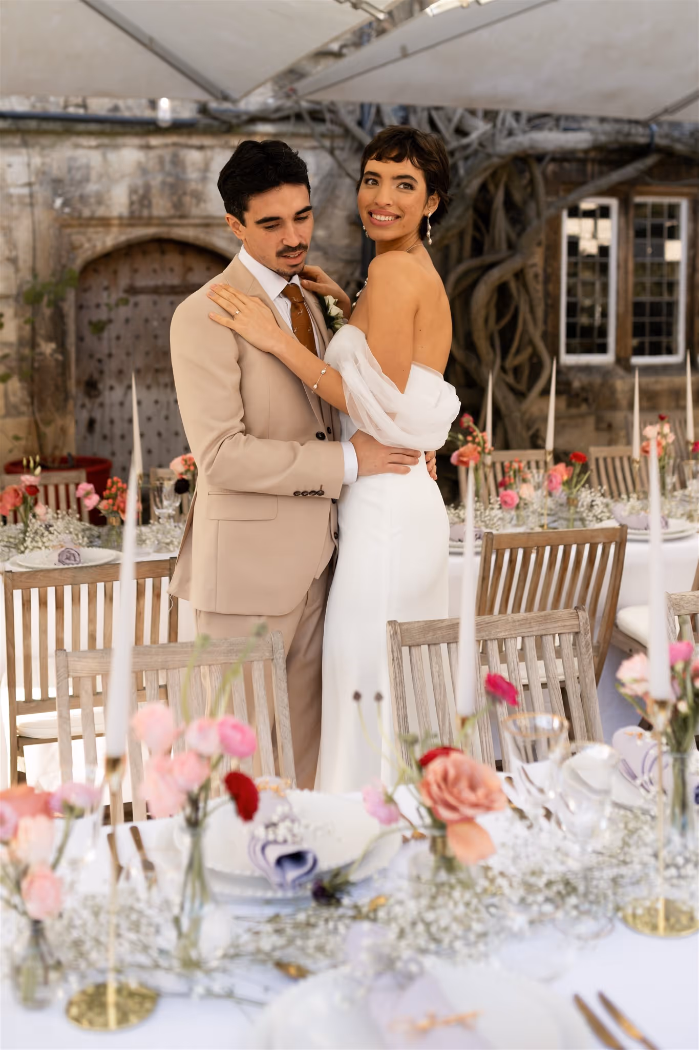 Bride in wedding dress and groom embracing looking at their wedding breakfast dining set up 