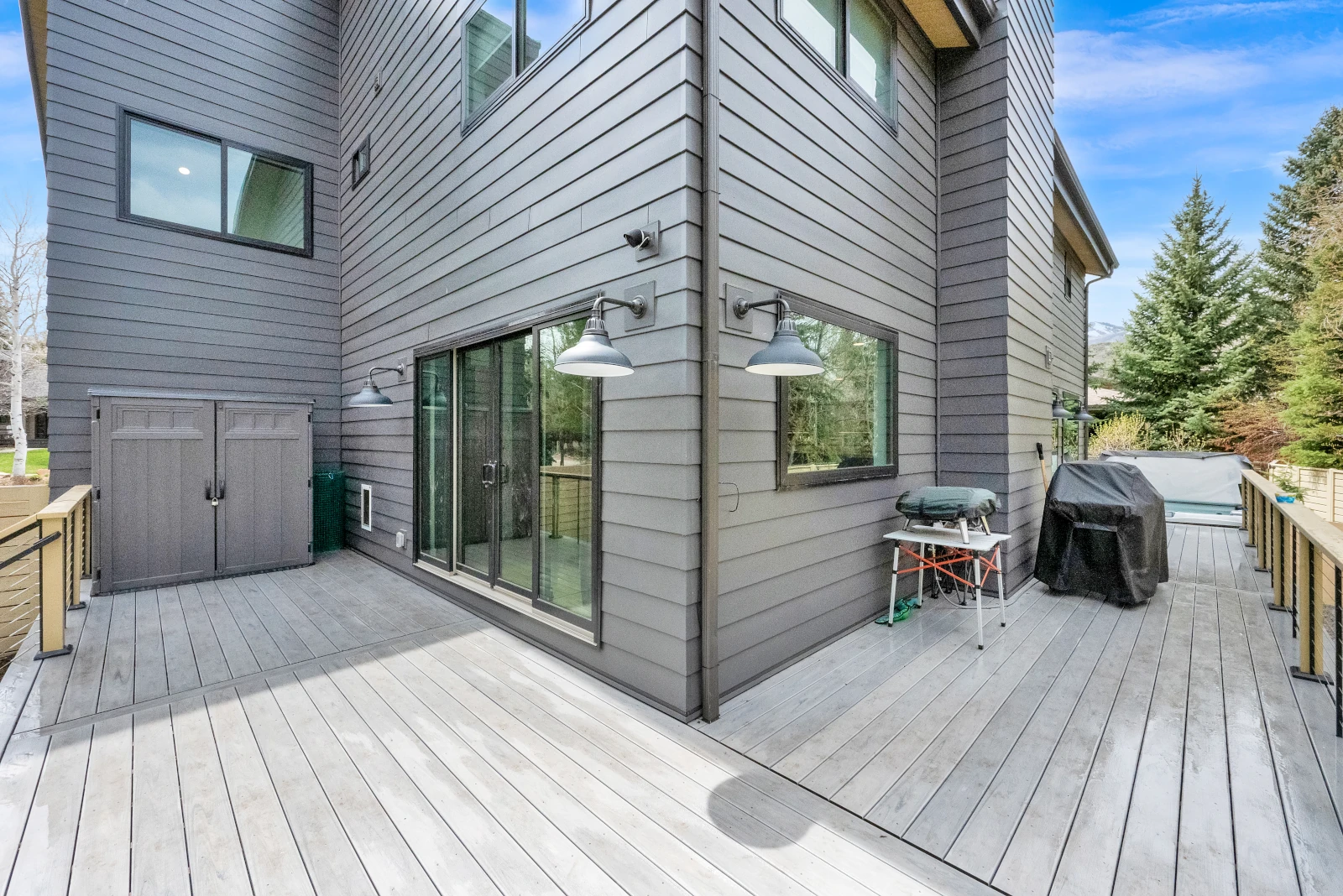 Composite deck wrapping the rear corner of a gray-sided home with cable railing, grill station, and covered hot tub