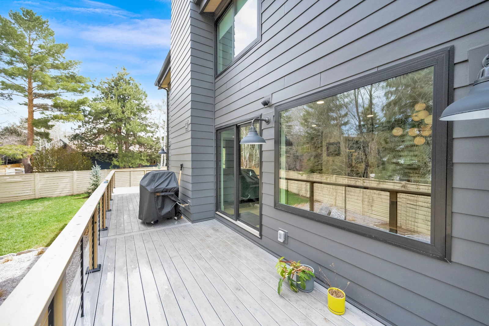 Gray composite deck beside a modern home with a large picture window and sliding door, overlooking a fenced lawn