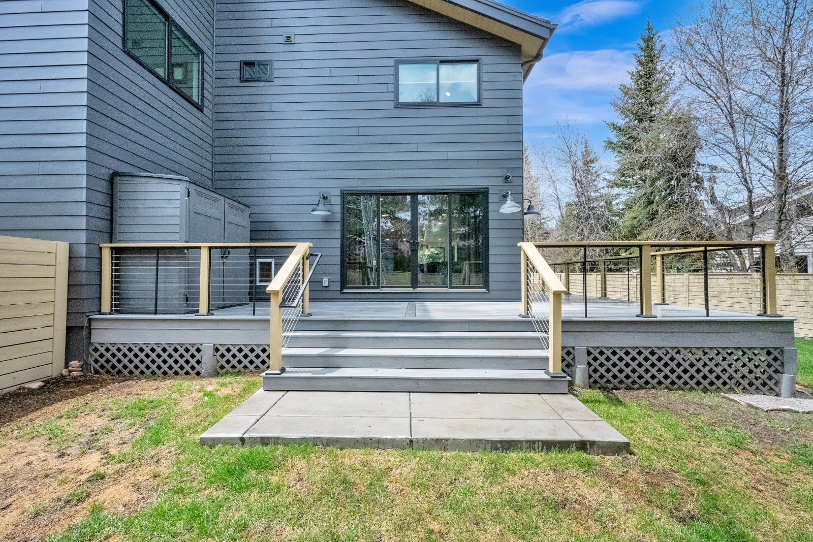 Composite deck with wide stairs down to a concrete pad, cable railing, and sliding glass doors at the rear entry