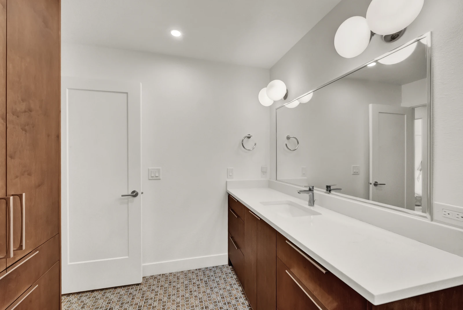 Bathroom remodel vanity with long quartz counter, full-width mirror, globe sconces, and walnut cabinetry