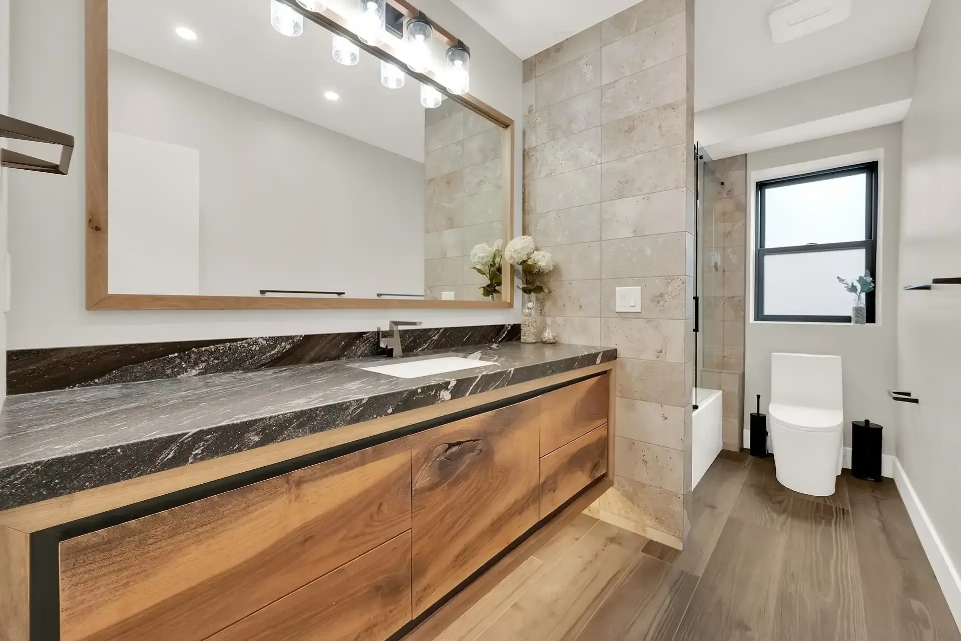 Contemporary bathroom featuring wood plank flooring, a floating vanity, and large framed mirror.