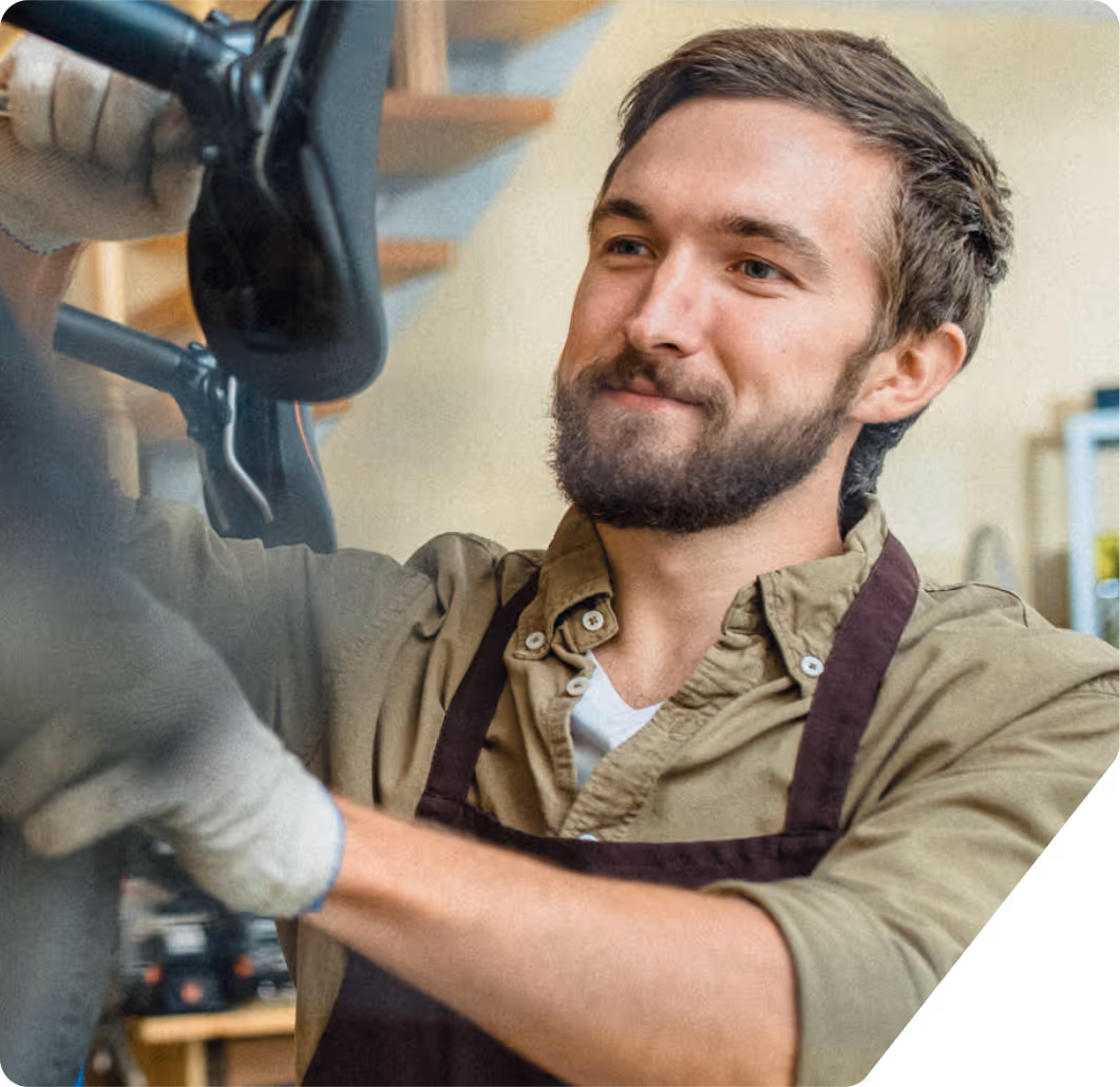 Bearded man in apron repairing or adjusting a bicycle in a workshop.