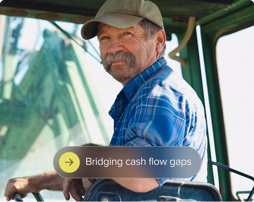 Older man wearing a cap and blue plaid shirt sitting in a tractor cabin.