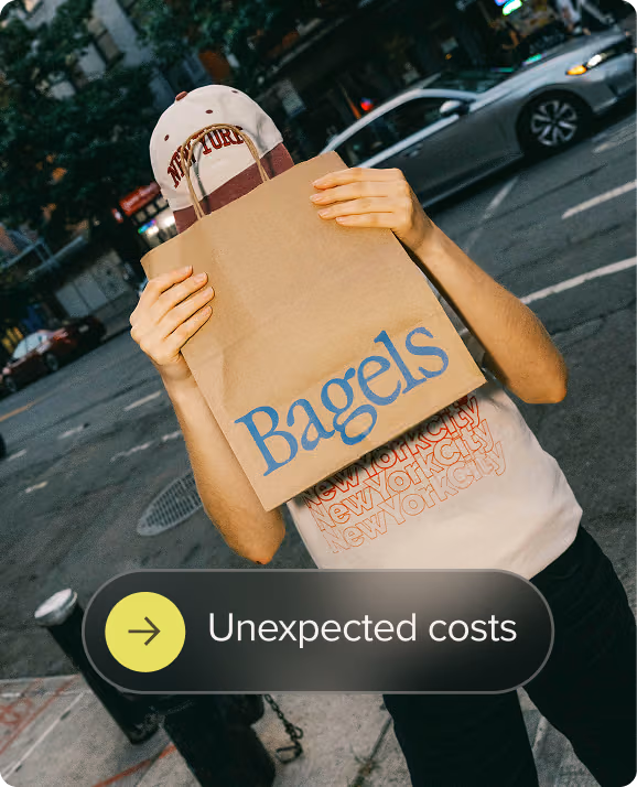 Person on city street covering their face with a paper bag labeled Bagels.