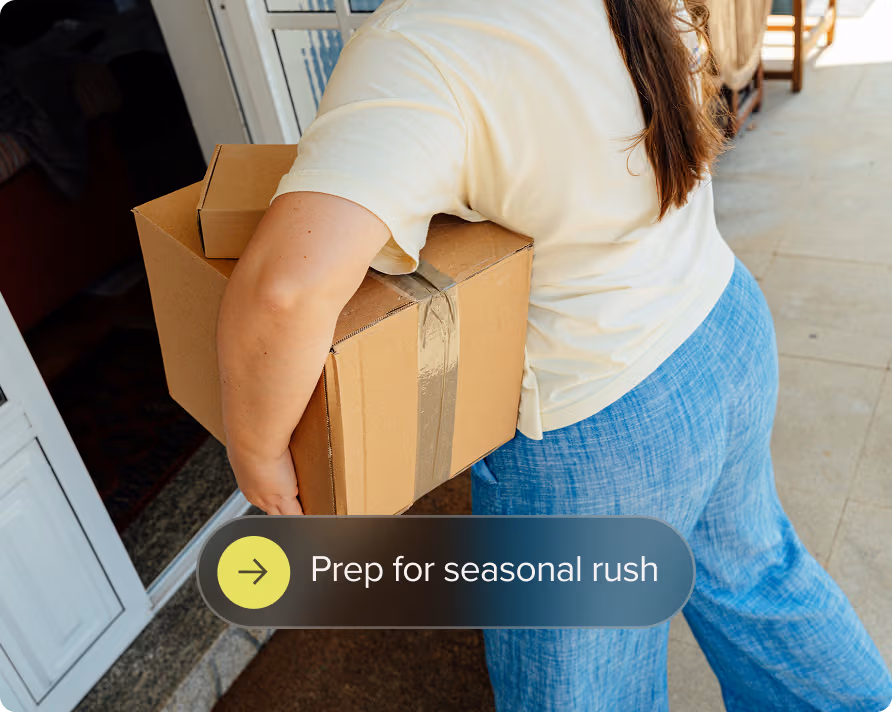 Person carrying two taped cardboard boxes entering a doorway, viewed from behind.