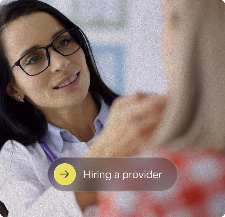 A female healthcare provider with glasses and a stethoscope gently touching the shoulder of a patient wearing a red garment with white patterns, conveying care and attention.