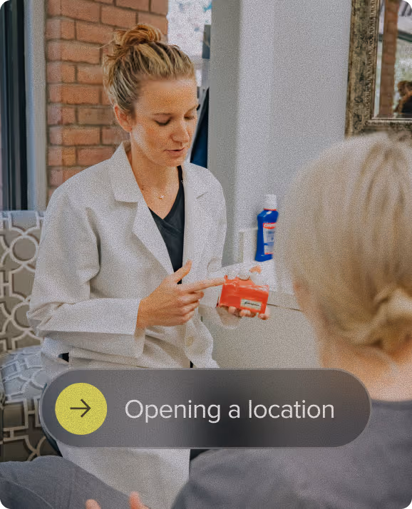 A woman in a white coat explaining a dental model to a seated person in a consultation setting.