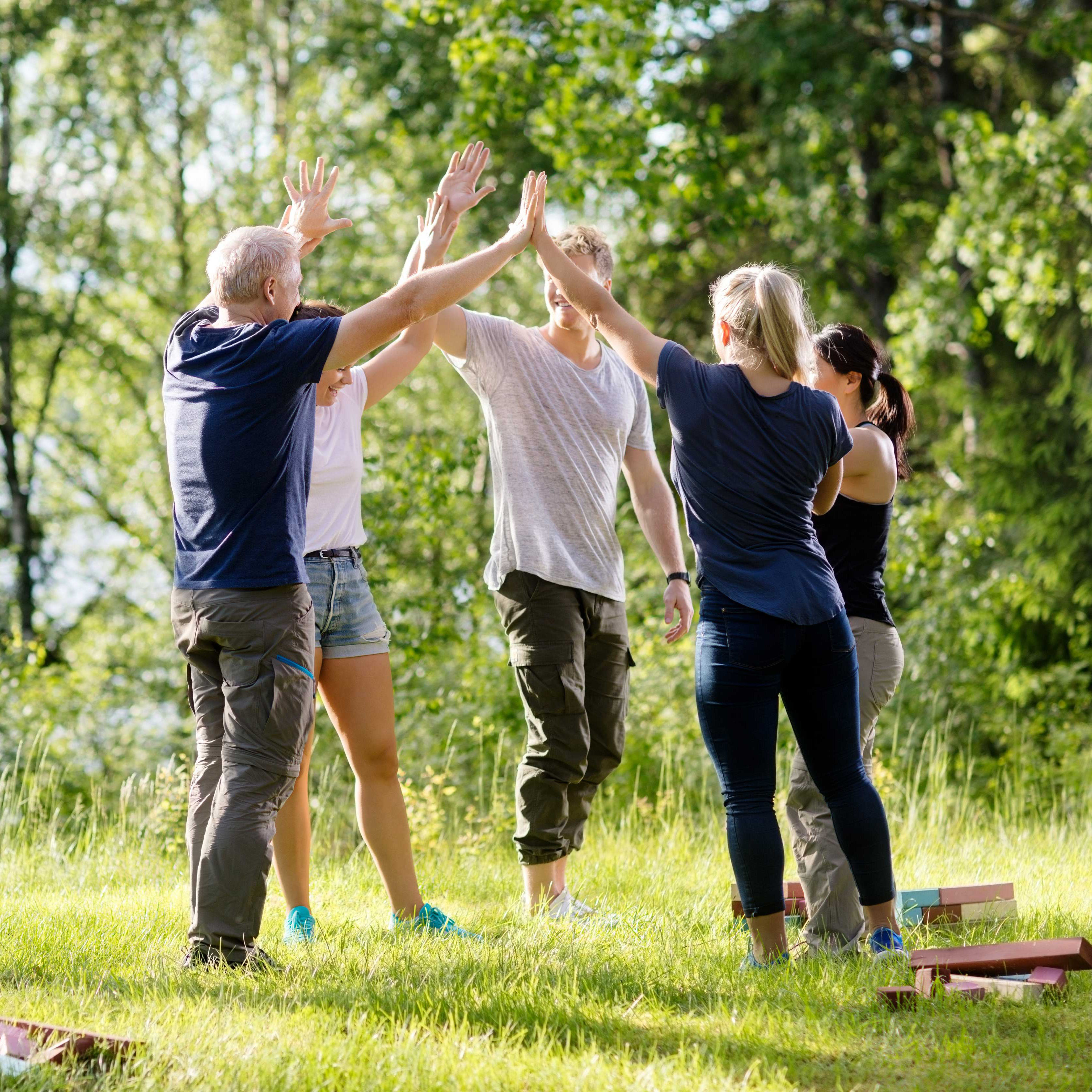 Fünf Personen geben sich draußen im grünen Park bei sonnigem Wetter gegenseitig High-Fives.