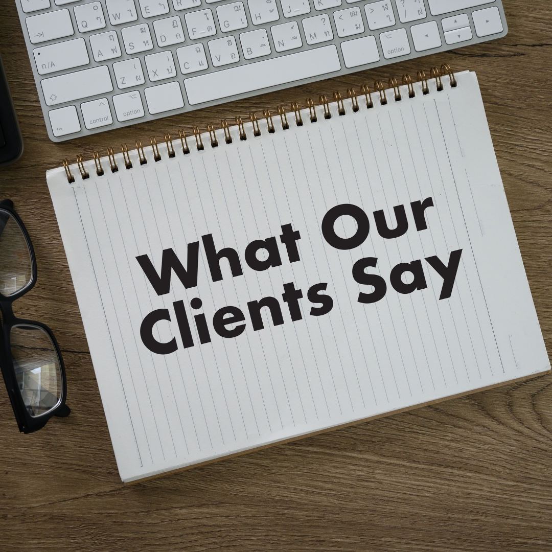A keyboard and notebook on a desk. The notebook says "What Our Clients Say"