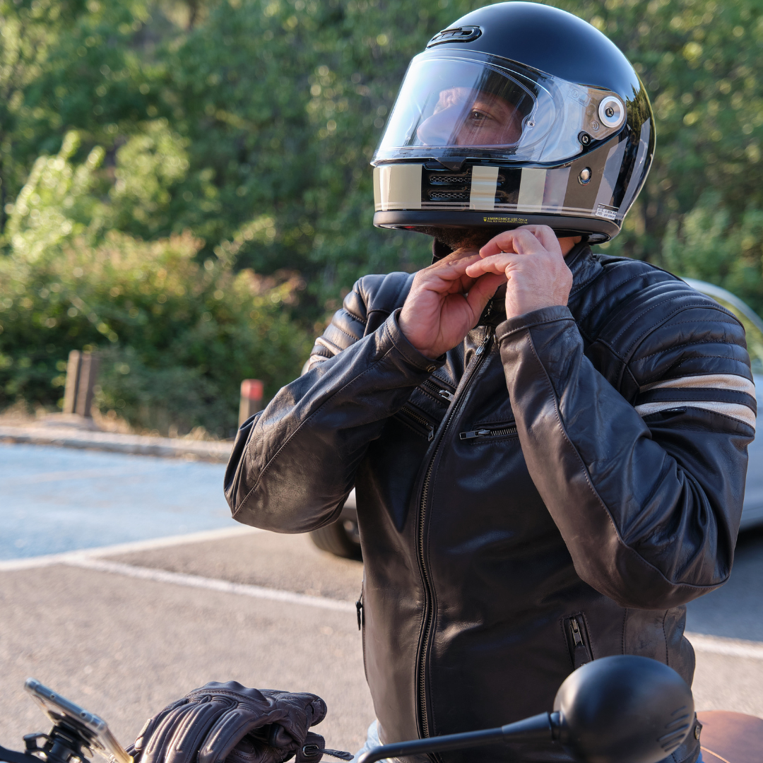 A motorcycle rider in a leather jacket strapping on his helmet