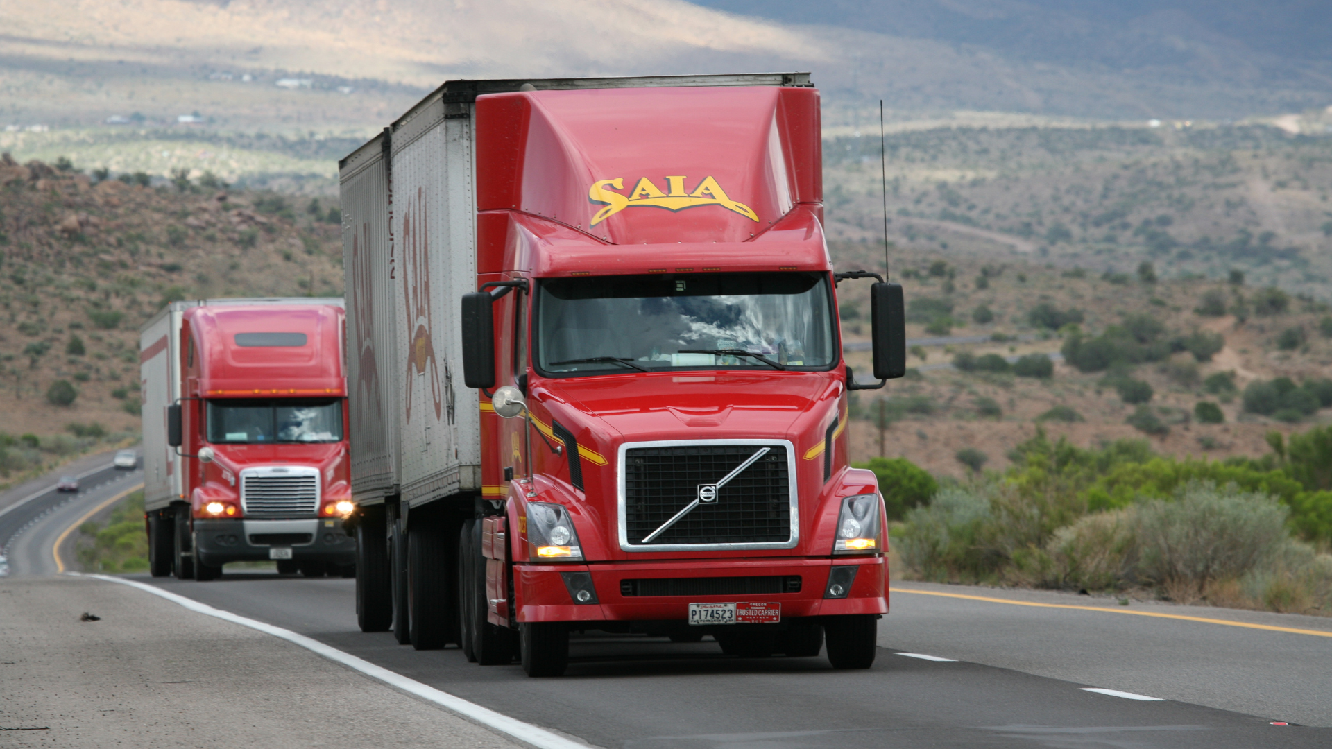 Two red semi trucks hauling trailers on a freeway