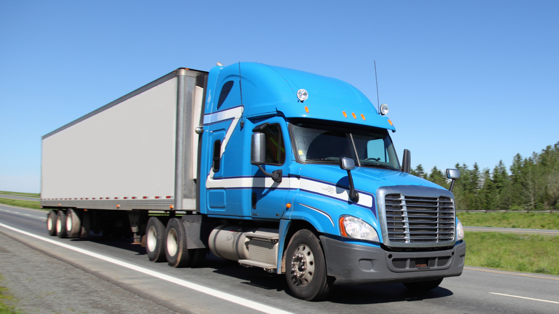 A blue and white semi truck hauling a trailer on a freeway during the daytime