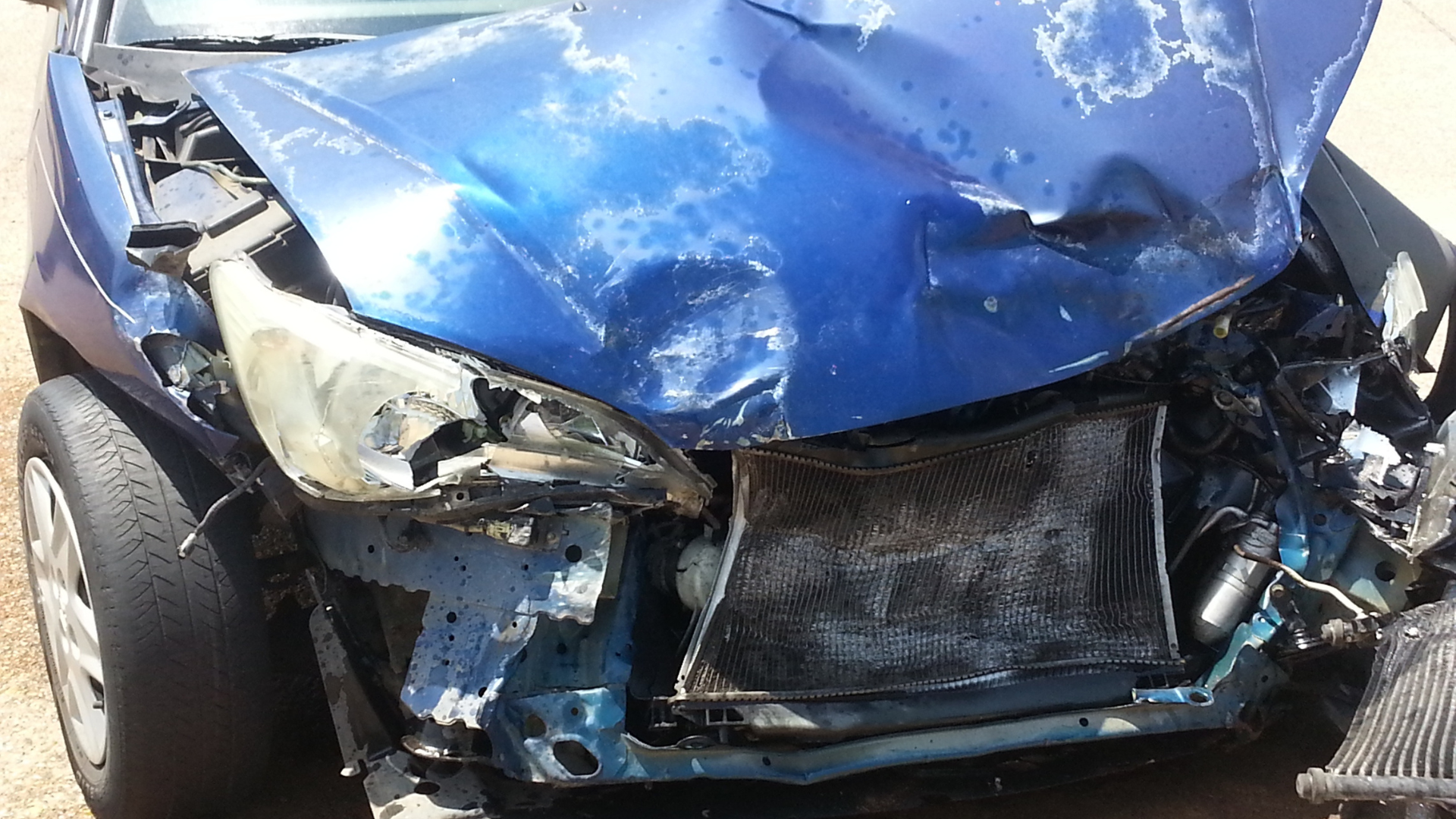 The damaged front end of a blue car after a collision