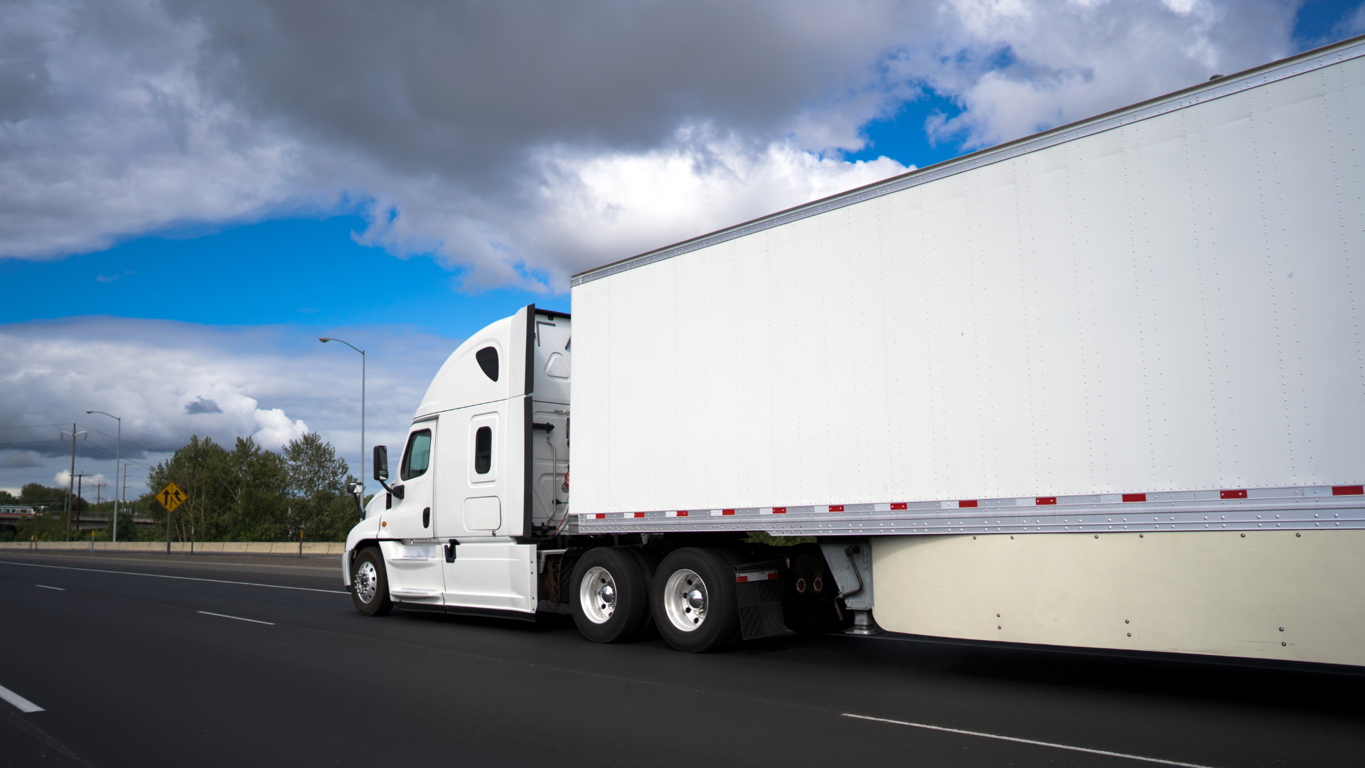 A white semi truck hauling a white trailer on a freeway