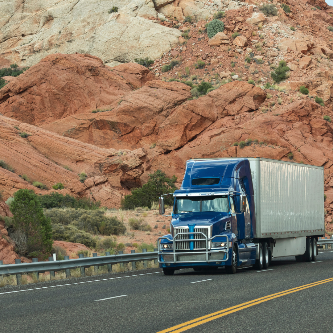 A blue semi truck hauling a white trailer on a mountain freeway