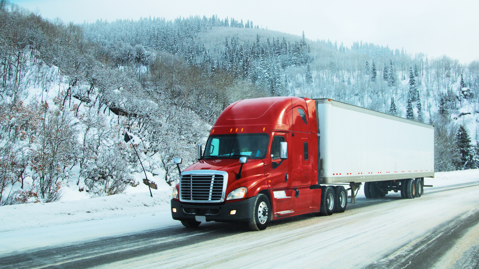 A red semi truck hauling a white trailer on Snoqualmie Pass