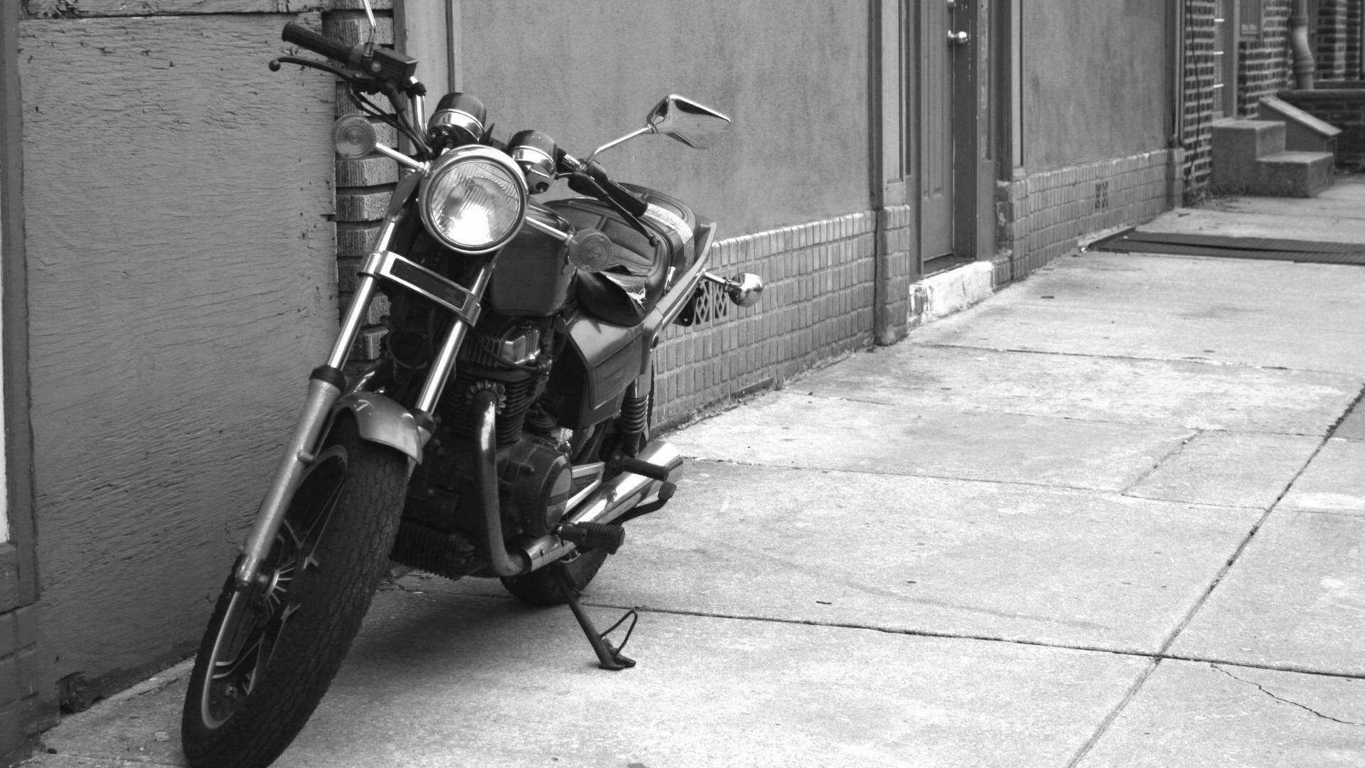 a black and white image of a motorcycle parked on a sidewalk alongside a building