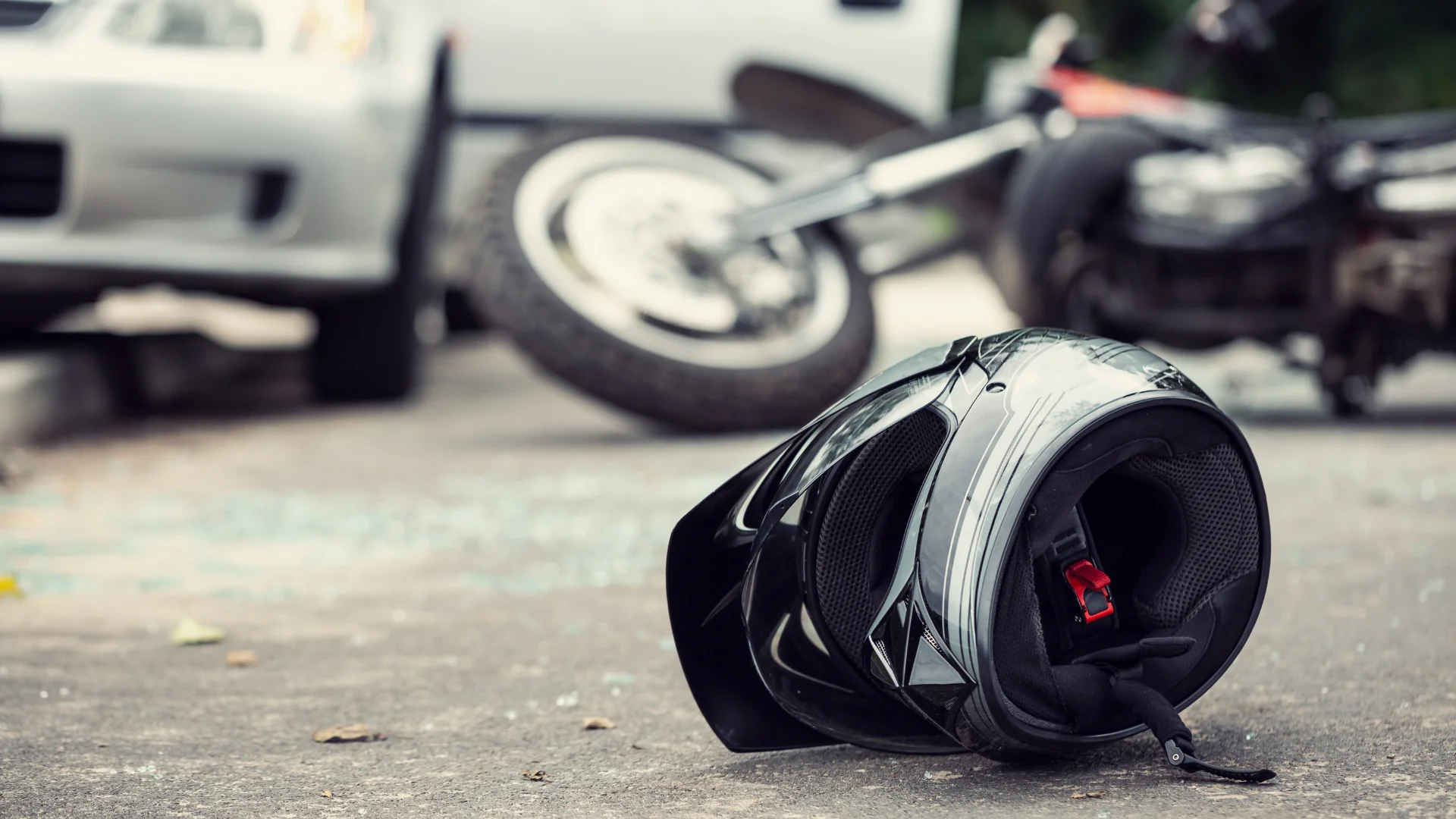 A motorcycle helmet on the ground with the aftermath of a motorcycle crash in the background
