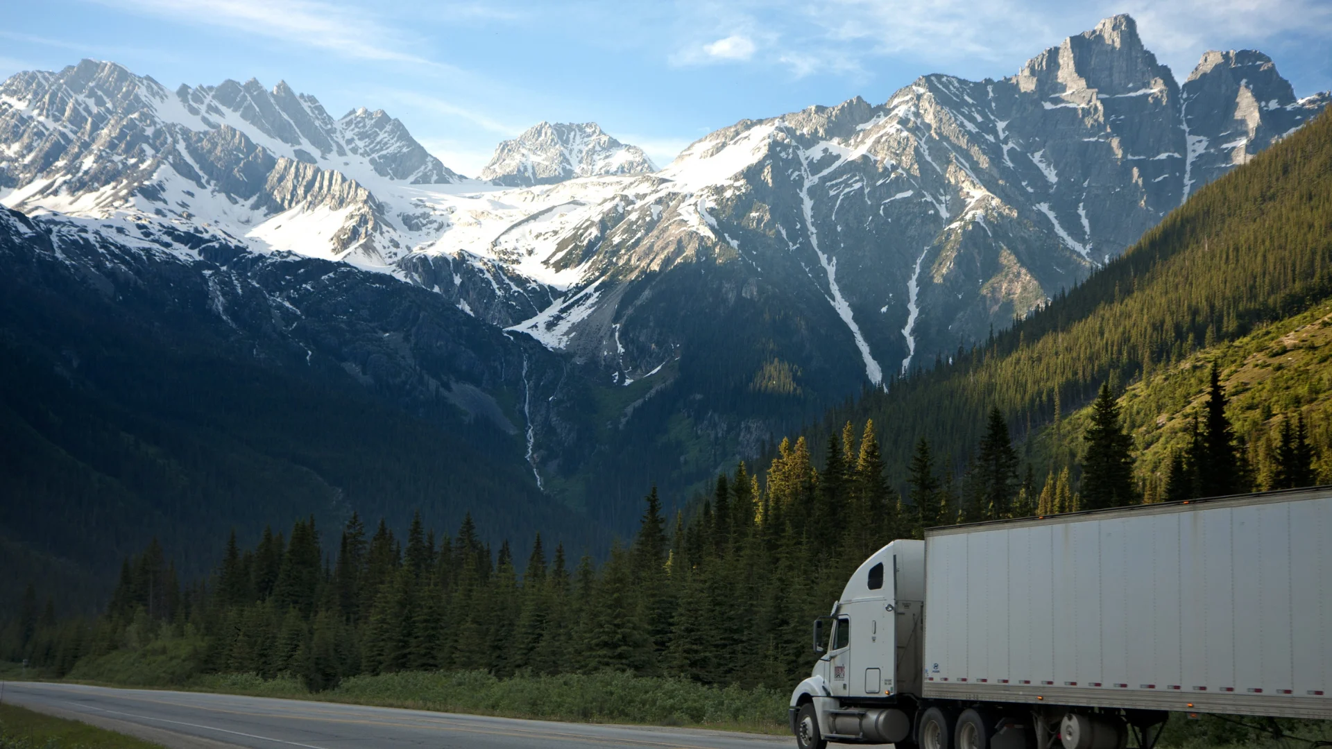 A white semi truck pulling a white trailer on a mountain highway