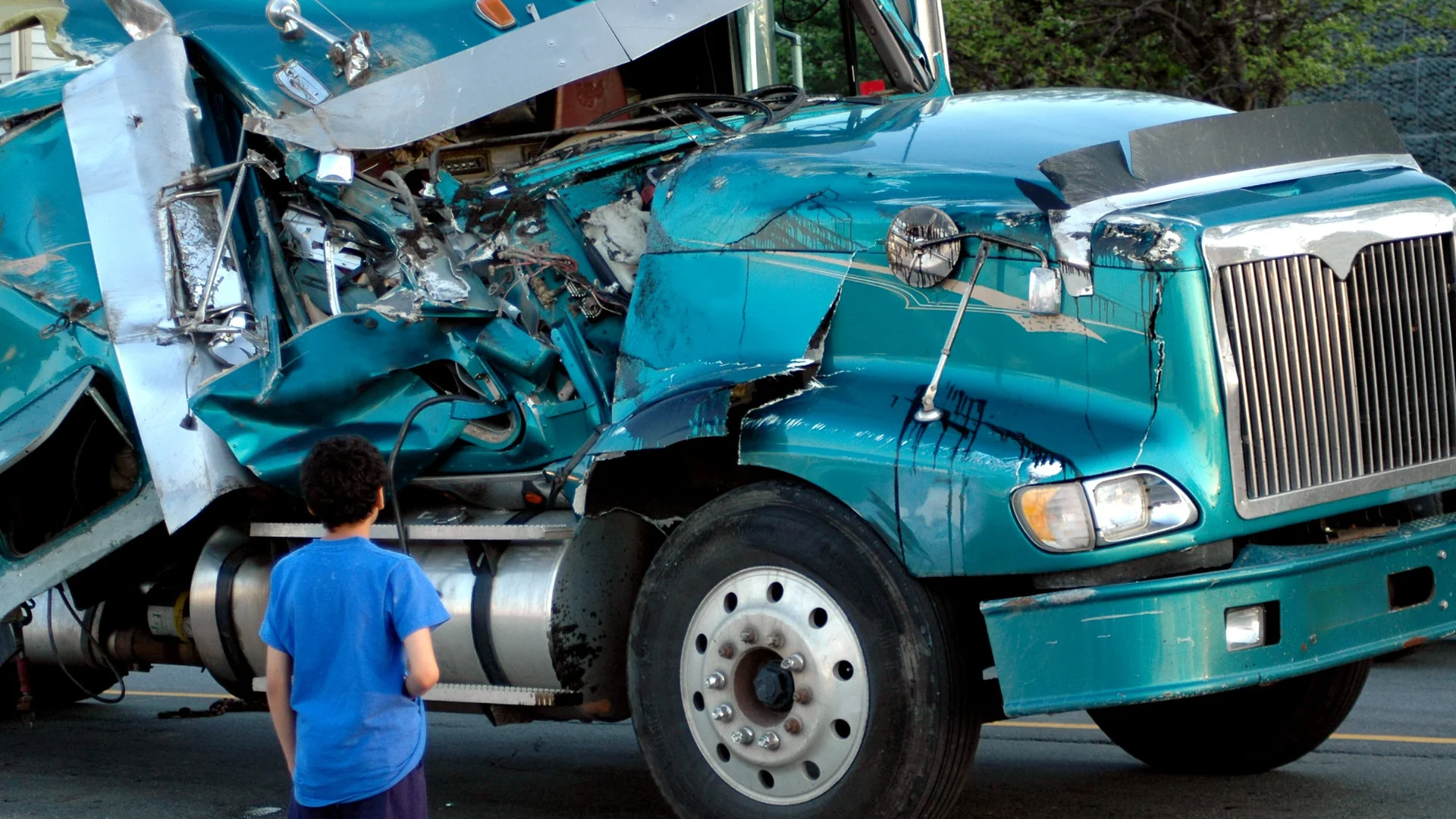A green semi truck that has been in a crash with severe damage to the passenger side
