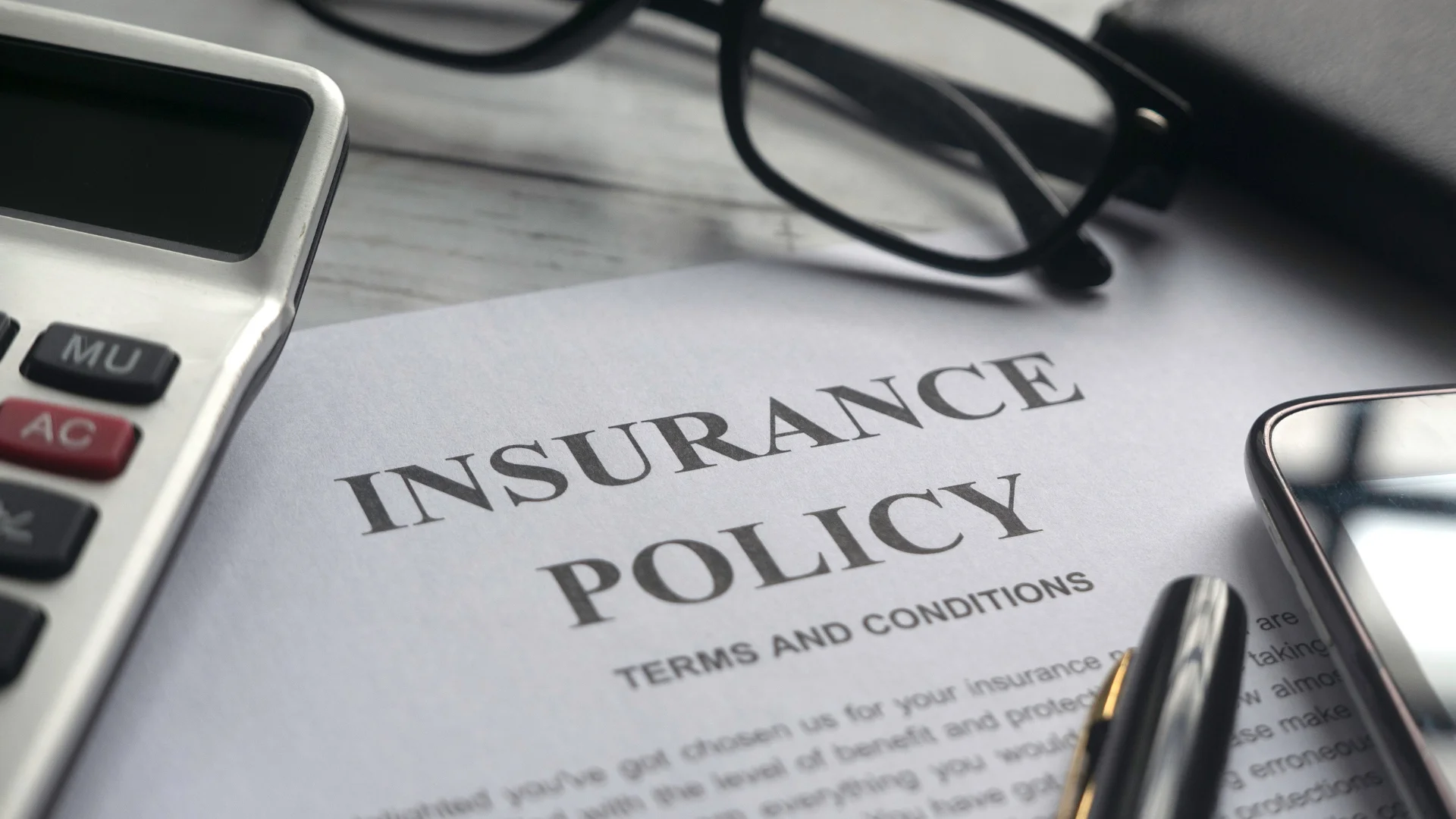 A picture of an insurance policy on a desk with a calculator, glasses and notebooks