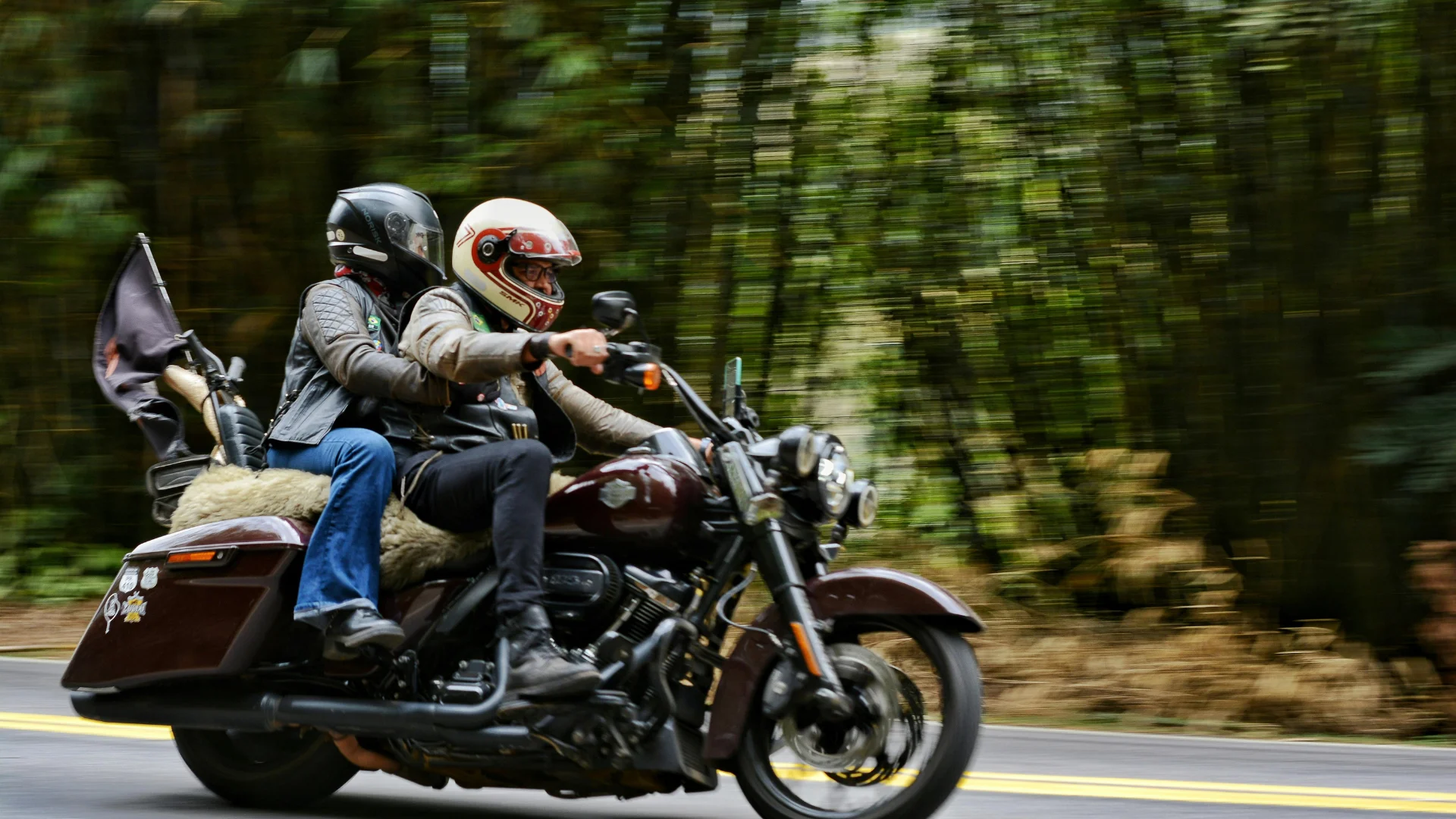 Two people riding a motorcycle through a forest