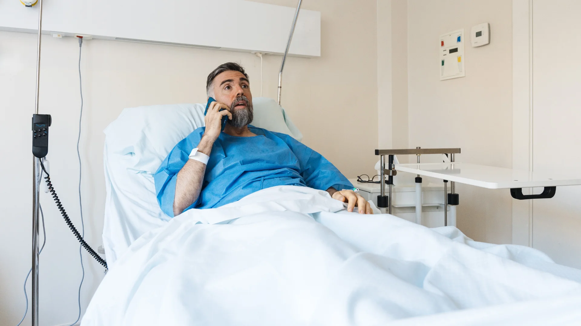 A man talking on a cell phone from a hospital bed