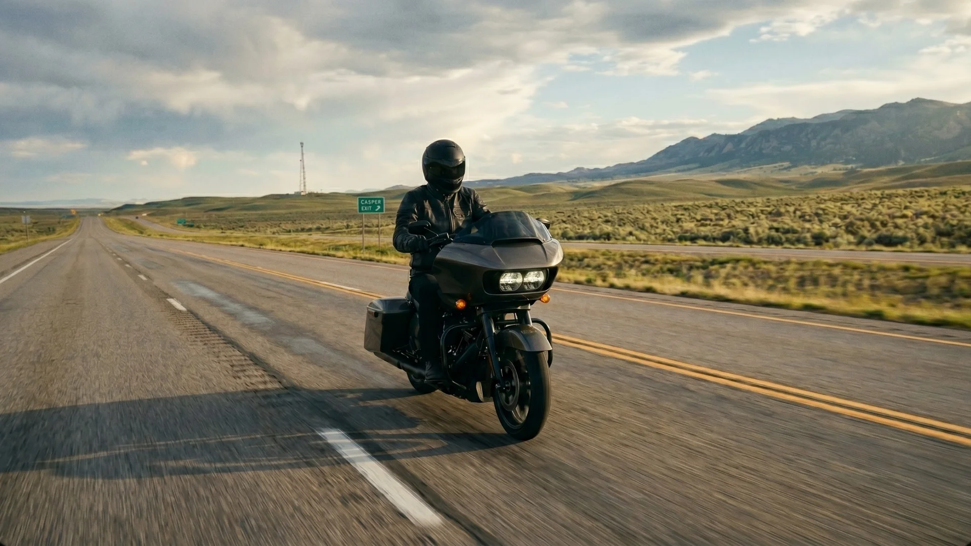 A motorcyclist wearing all black safety gear riding a black Harley-Davidson motorcycle on a rurall highway near Casper, Wyoming