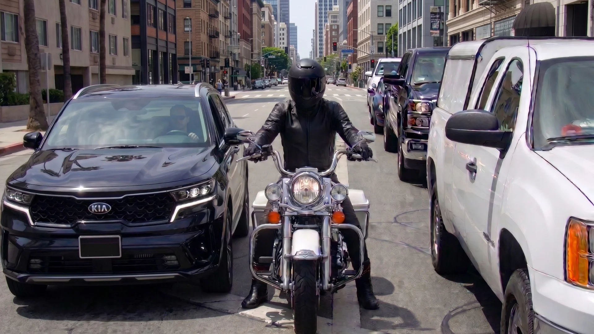 A motorcyclist in between 2 rows of cars stopped at an intersection, showing what proper lane filtering looks like.