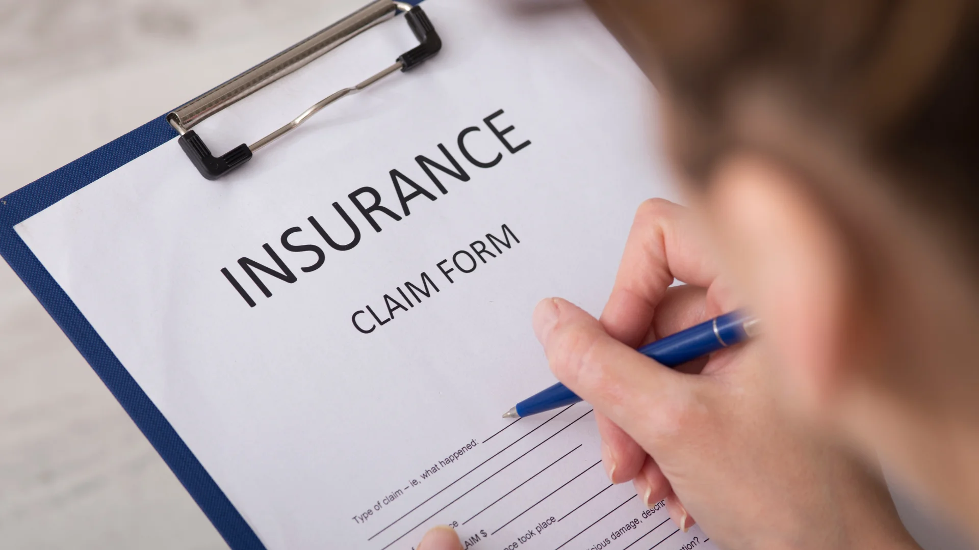 An insurance claim form on a clipboard with a person filling out information on it