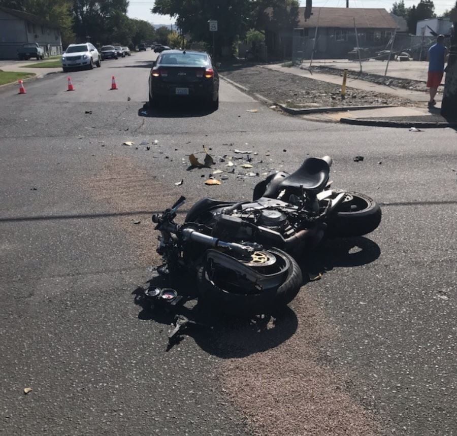 A motorcycle that is laying in the road after being hit by a car with debris on the road