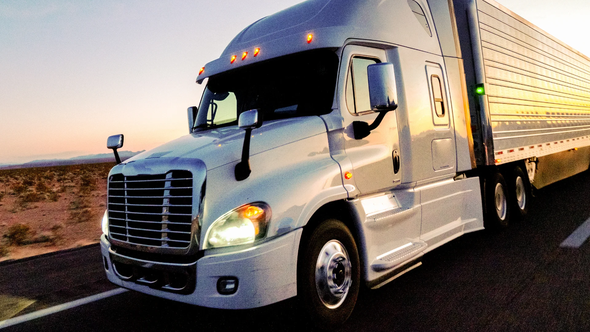 A white semi truck hauling a trailer on a highway at sunset