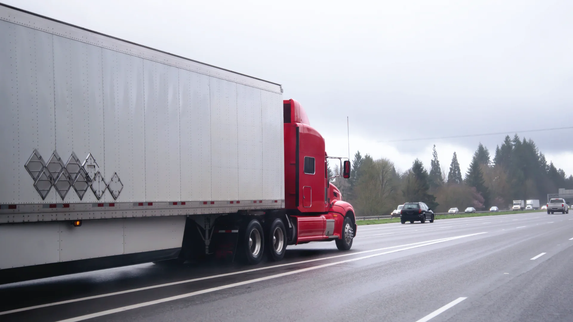 A red semi truck hauling a white trailer on a freeway in Washington