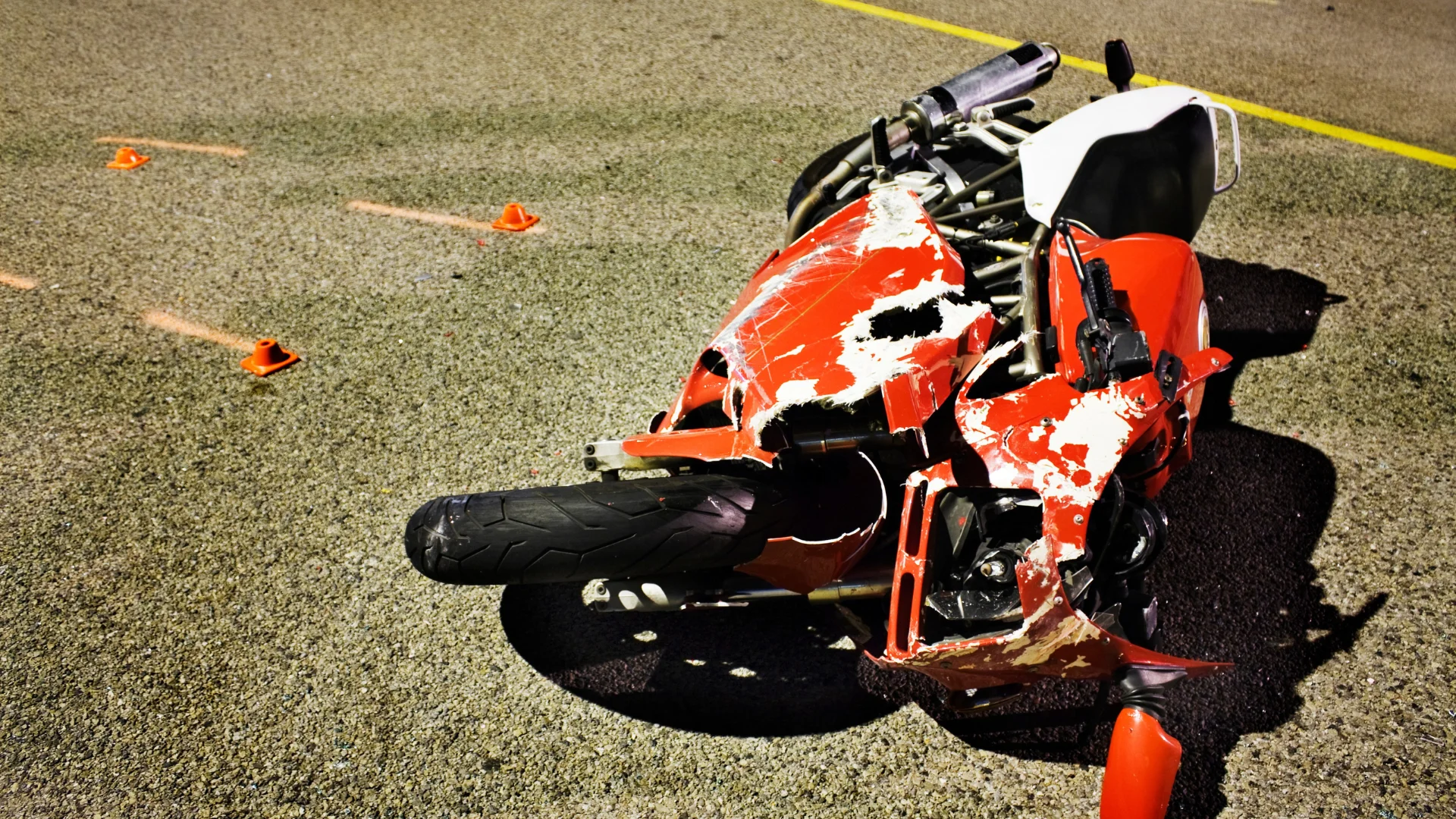A damaged red motorcycle laying on its side with accident markers on the ground nearby